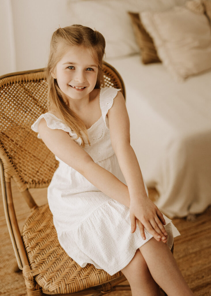 Lächelndes Mädchen in weißem Kleid auf Korbstuhl beim Familien-Fotoshooting